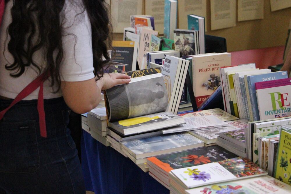 Una visitante hojea un libro ilustrado apoyado sobre una mesa cubierta de novedades, en uno de los stands.