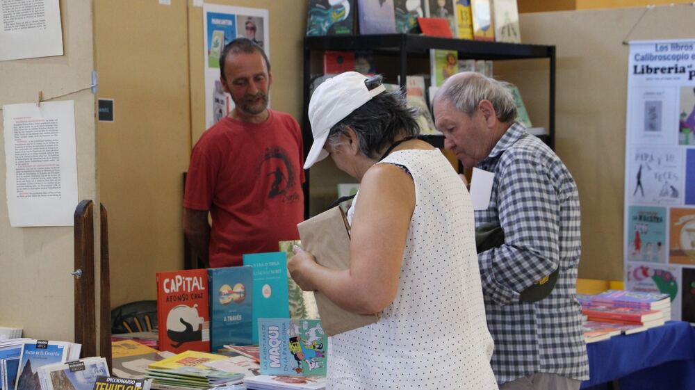 Tres personas miran libros de la Patagonia y libros infantiles en el stand de una librería.